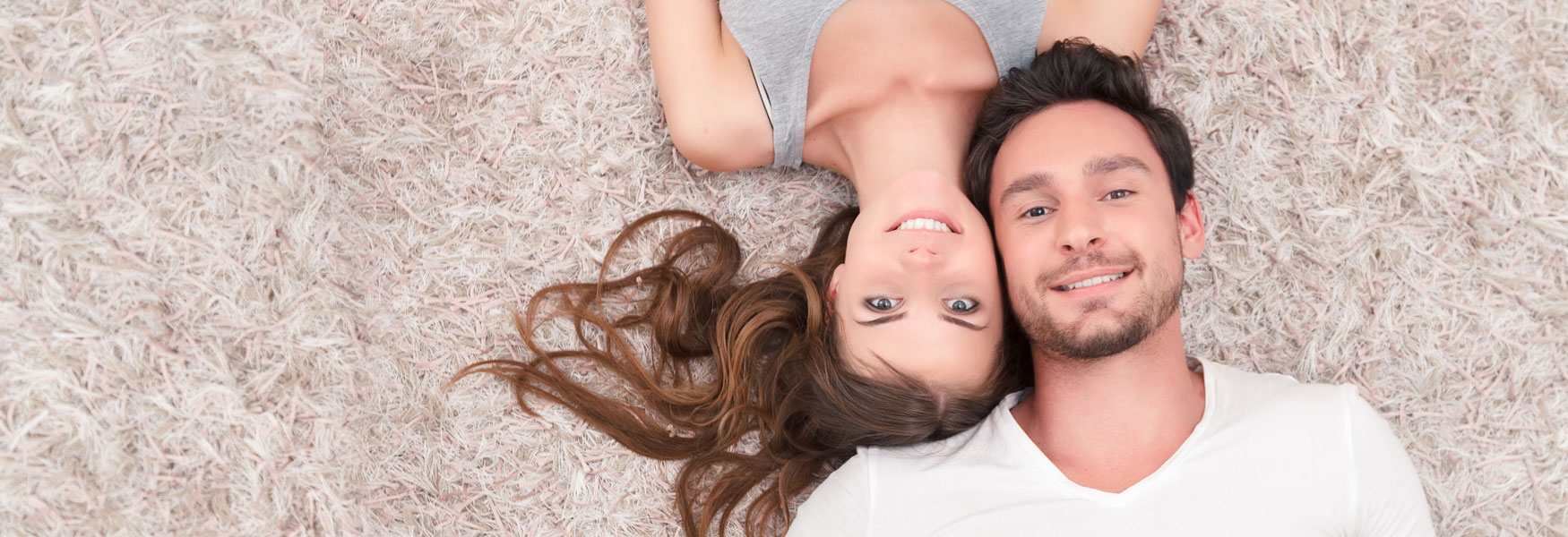 Smiling couple lay down on floor facing up.